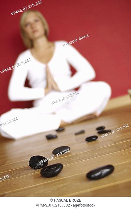 Close-up of pebbles with a young woman sitting in a prayer position in the background