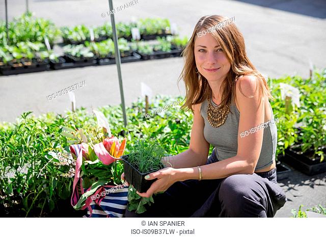 Woman at fruit and vegetable stall holding herb plants