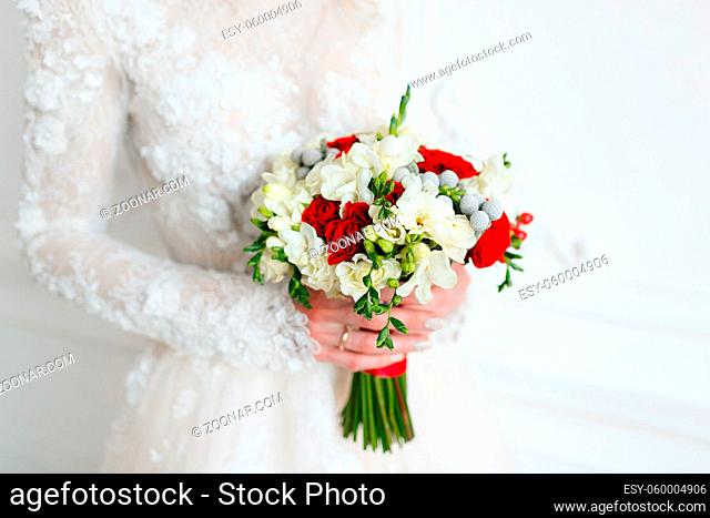 Bride holding bridal bouquet close up. red and white roses, freesia, brunia decorated in composition