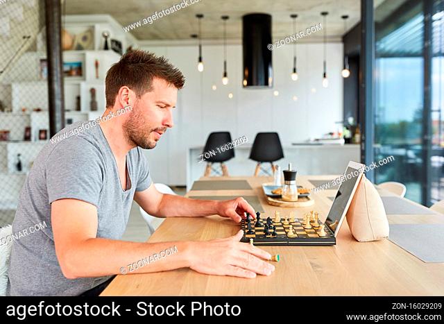 Junger Mann beim Schach spielen im Videochat online zu Hause im Wohnzimmer