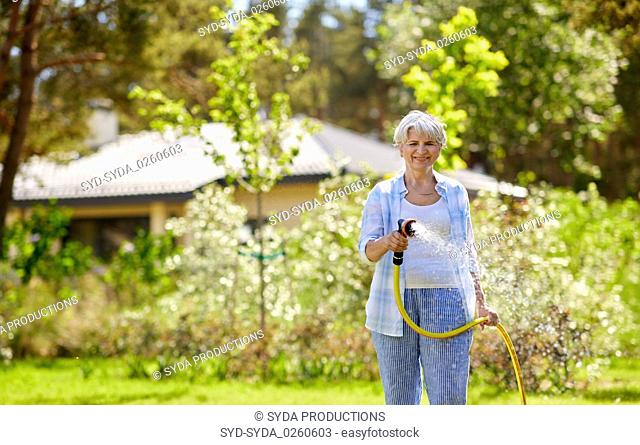 senior woman watering lawn by hose at garden