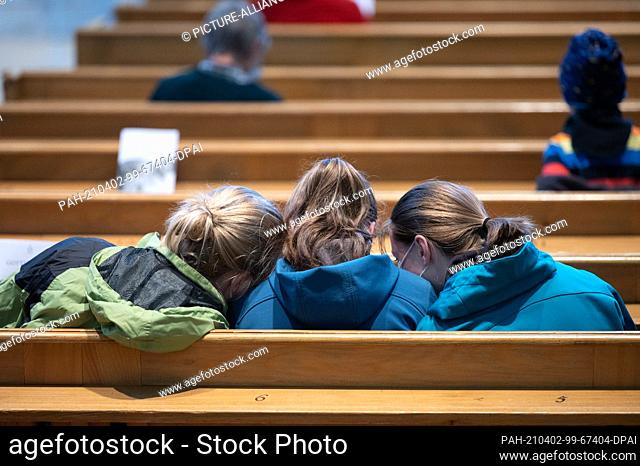 02 April 2021, Saxony, Dresden: Young visitors sit next to each other on a pew before the start of a Good Friday service in the Frauenkirche