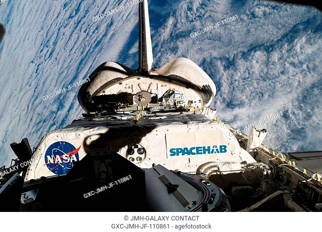 Backdropped by a cloud-covered part of Earth, the SPACEHAB pressurized logistics module in Space Shuttle Endeavour's payload bay and vertical stabilizer are...