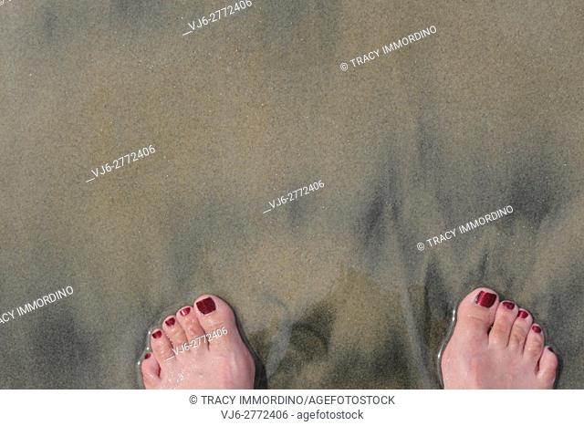 Close up of two feet with painted toenails in the tan and black sand at Torrey Pines Natural Reserve in San Diego, California, USA