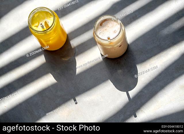 Couple of colorful cocktails with fruit slices in glass jars with white-cyan straws on the gray table. Sun shines onto them and creates shadows