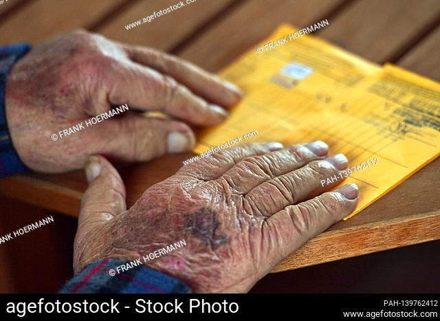 Wrinkled hands of an old man (92 years old) lie on his vaccination certificate after vaccination, corona vaccination versus SARS-CoV-2