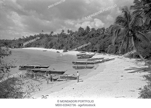 Tourists on a beach of Zanzibar with many moored pirogues. Zanzibar, 1950s