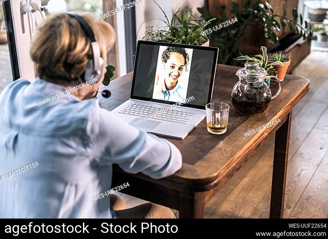 Senior woman having video call with granddaughter through laptop on table in living room