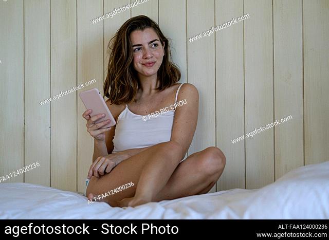 Young woman using smartphone in bedroom