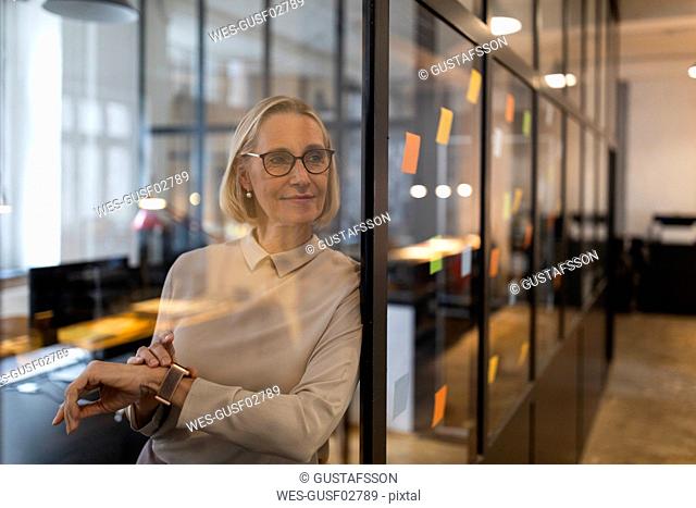 Mature businesswoman looking at adhesive notes on glass pane in office