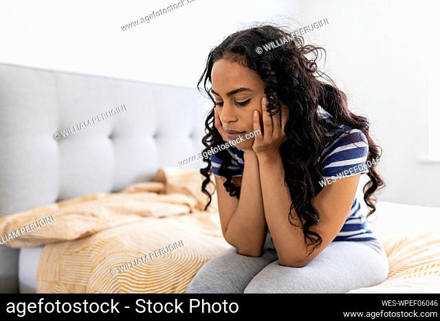 Sad woman with hand on chin in bedroom