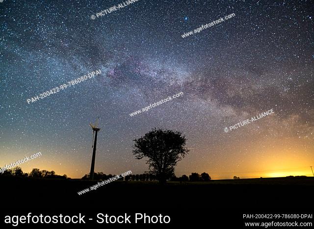 22 April 2020, Schleswig-Holstein, Neukirchen: The starry sky shines above a tree and a windmill. Mostly starry skies currently allow a clear view of the...