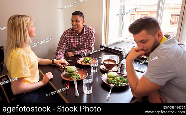 Picture of happy couple looking at each other while their friend sitting sad in front of them in vegan restaurant or cafe