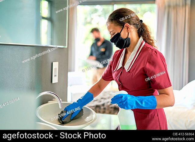 Female hotel maid in face mask and gloves cleaning hotel room bathroom