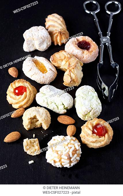 Different sorts of Italian almond cookies and a pastry tong on slate