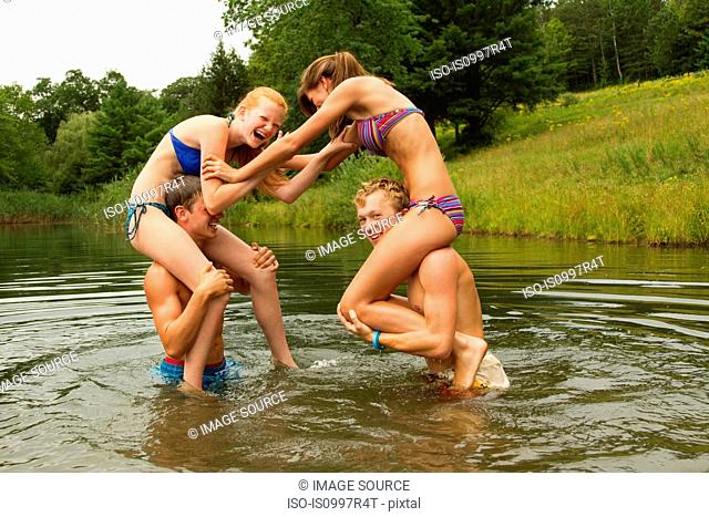 Teenage girls sitting on boys' shoulders in lake