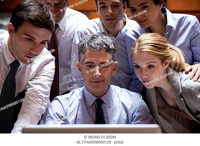 Business associates crowd around colleague looking over his shoulder at laptop computer
