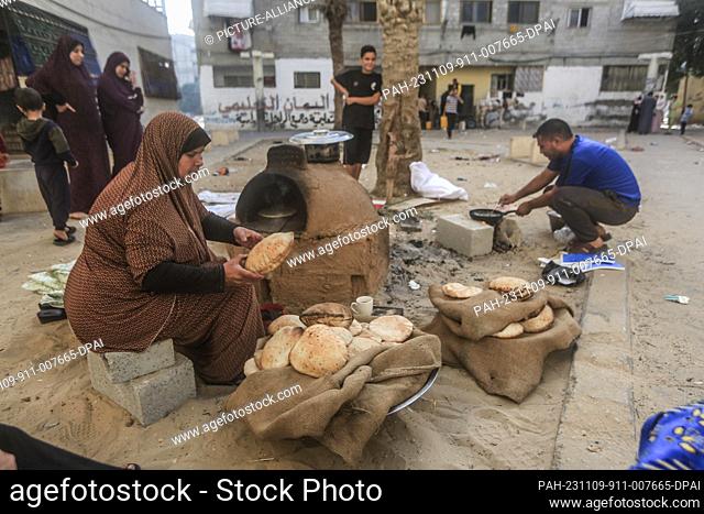 09 November 2023, Palestinian Territories, Khan Yunis: A Palestinian woman bakes traditional bread near a UNRWA school gate
