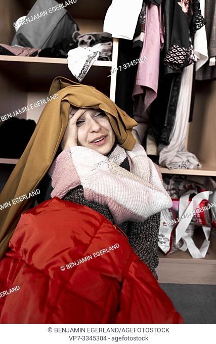 young woman overwhelmed by her clothes, in front of wardrobe