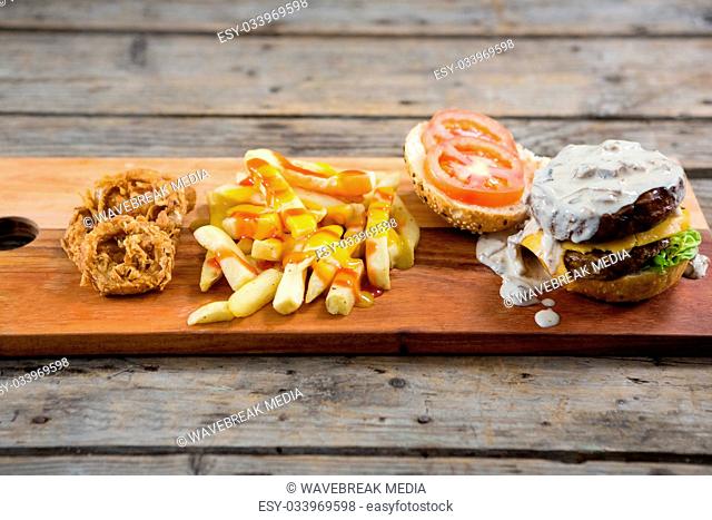 French fries with sauce by onion rings and burger on cutting board
