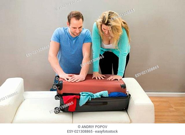 Couple Together Trying To Close Their Luggage