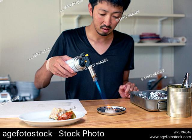 A chef preparing plates of Italian food in a restaurant. using a blow torch to heat a dish