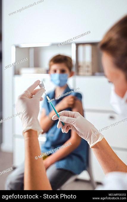 Nurse preparing vaccine injection for boy in background