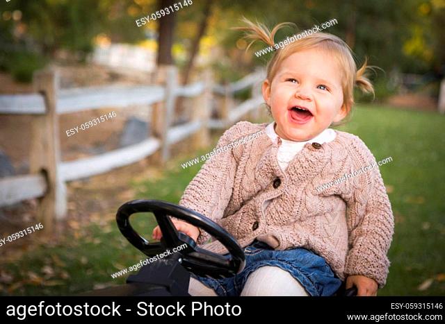 Happy Young Toddler Laughing and Playing on Toy Tractor Outside