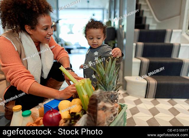 Cute baby daughter helping mother unpack grocery delivery