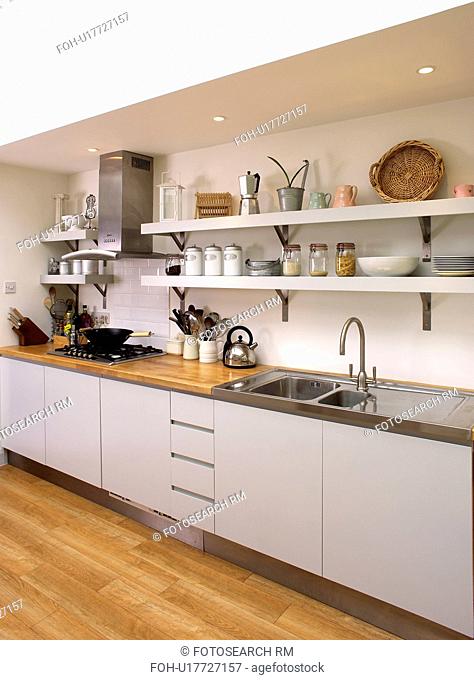 Stainless steel sink in fitted white unit below white shelves in modern kitchen