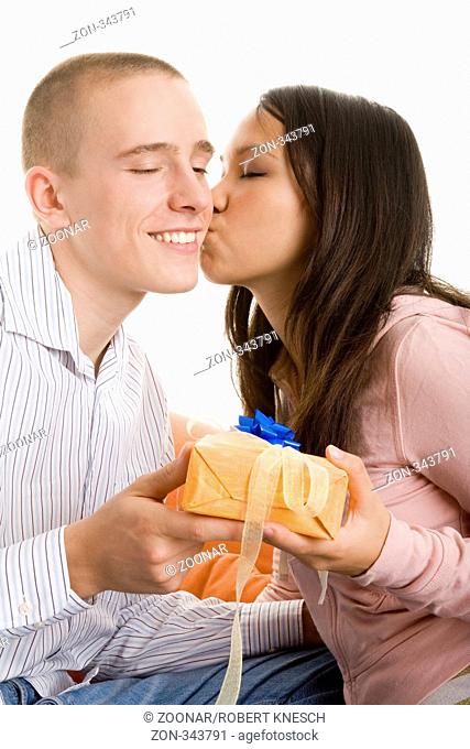 Junge Frau bedankt sich mit einem Kuss bei ihrem Freund, der ihr gerade ein Geschenk überreicht hat