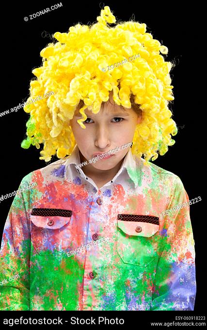 A funny boy in a yellow clown wig and colorful clothes with a sad face