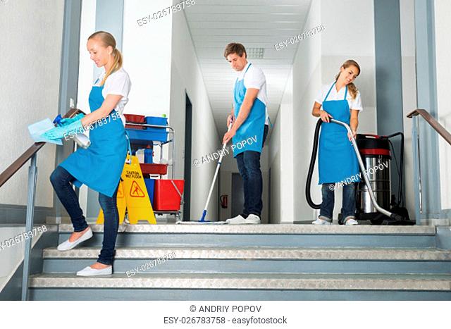 Group Of Happy Male And Female Janitor Cleaning Corridor With Cleaning Equipments