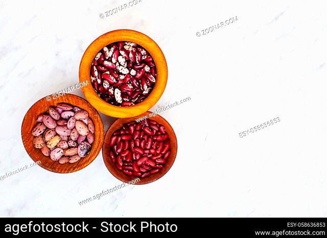Three types of kidney beans in wooden bowls on a white background