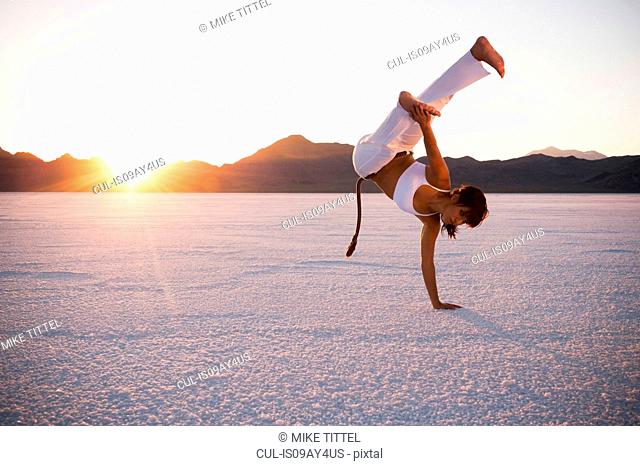 Woman performing capoeira on Bonneville Salt Flats at sunset, Utah, USA