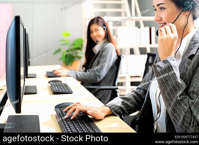Young adult friendly and confidence operator woman agent smiling with headsets working in a call center with her colleague team working as customer service and...