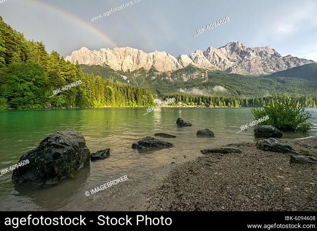Rocks on the shore, Eibsee lake in front of Zugspitze massif with Zugspitze with rainbow, behind thunderclouds, Wetterstein range, near Grainau, Upper Bavaria