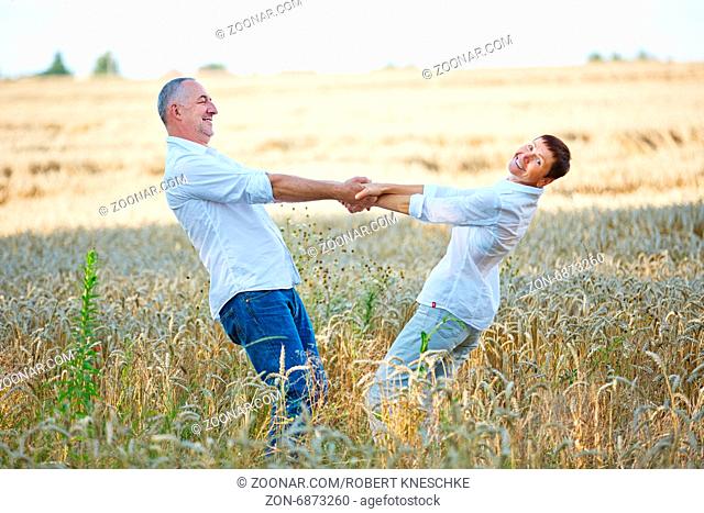 Glückliche Senioren tanzen gemeinsam im Sommer auf einem Feld voller Weizen
