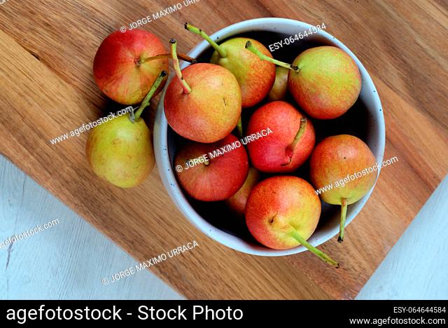 White bowl with small pears on wooden board