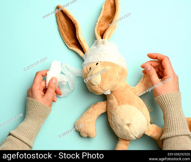 plush beige rabbit with a bandaged head with a white medical bandage on a blue background