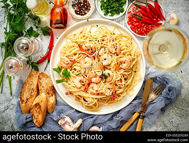 Spaghetti with shrimps on white ceramic plate and served with glass of white wine. Various fresh ingredients on sides. Top view, flat lay