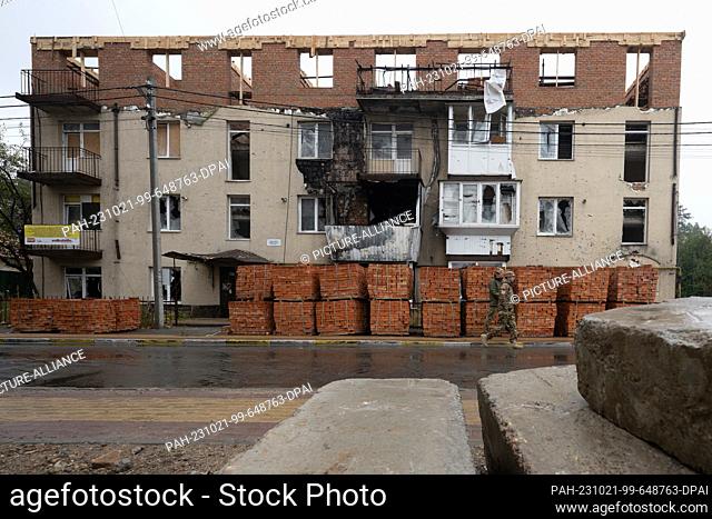 PRODUCTION - 20 October 2023, Ukraine, Irpin: Two men walk past bricks lying in front of a demolished house, which is being rebuilt