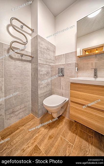 Modern tiled bathroom interior toilet seat and sink with brown tile and mirror
