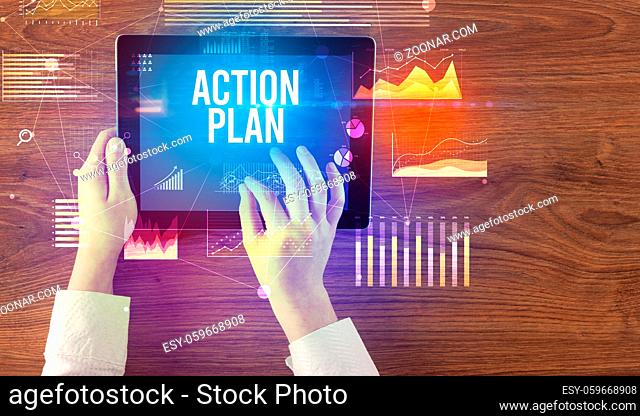 Close-up of hands holding tablet with ACTION PLAN inscription, modern business concept