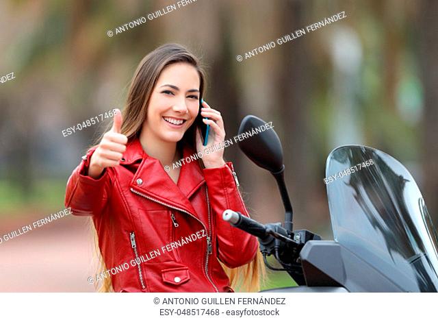 Happy biker sitting on a motorbike with thumbs up calling on phone on the street