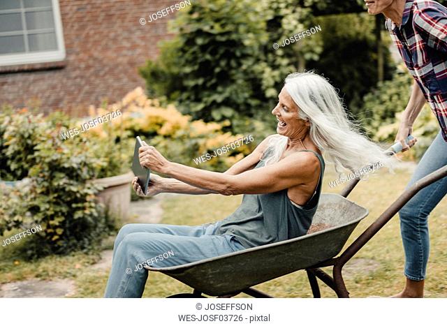 Senior woman sitting push cart, using digital tablet