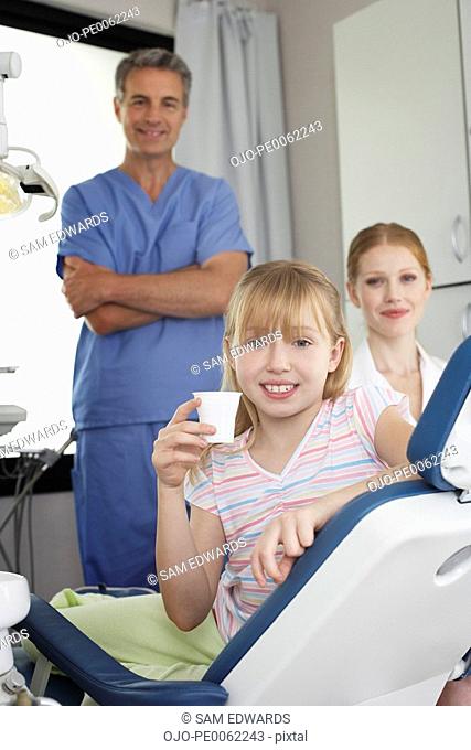 Dentist and dental assistant in examination room with smiling young patient in chair