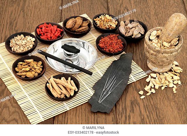 Acupuncture needles, moxa sticks, traditional chinese herbs for herbal medicine and mortar with pestle over bamboo and old oak background