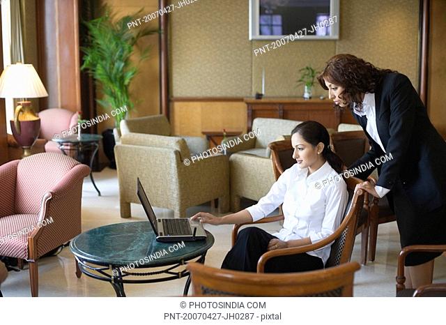 Side profile of two businesswomen looking at a laptop in a lobby