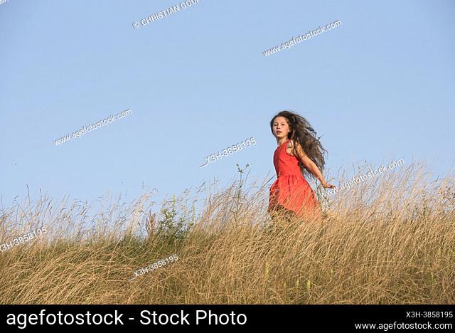 Jeune fille en robe rouge sur un talus herbeux, France, Europe / Girl in red dress on a grassy slope, France, Europe